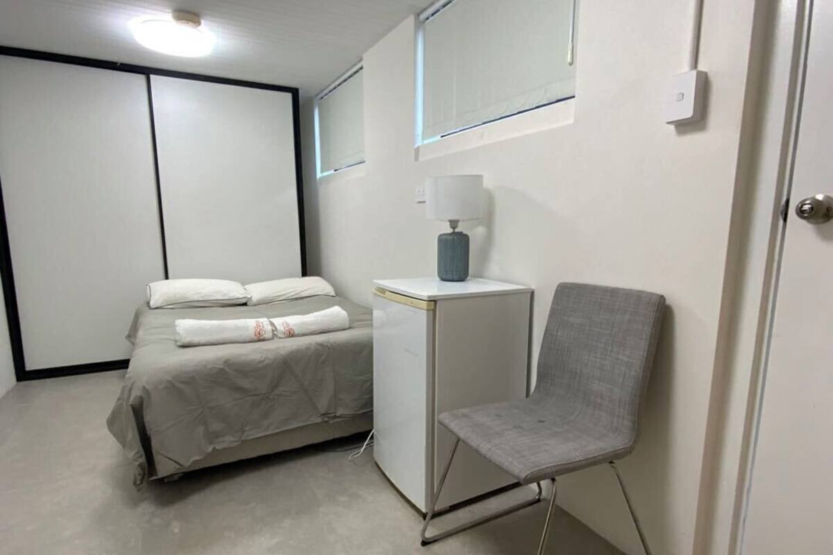 A small, modern bedroom with a bed, bedside table, chair, and a door.