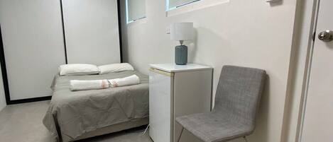 A small, modern bedroom with a bed, bedside table, chair, and a door.