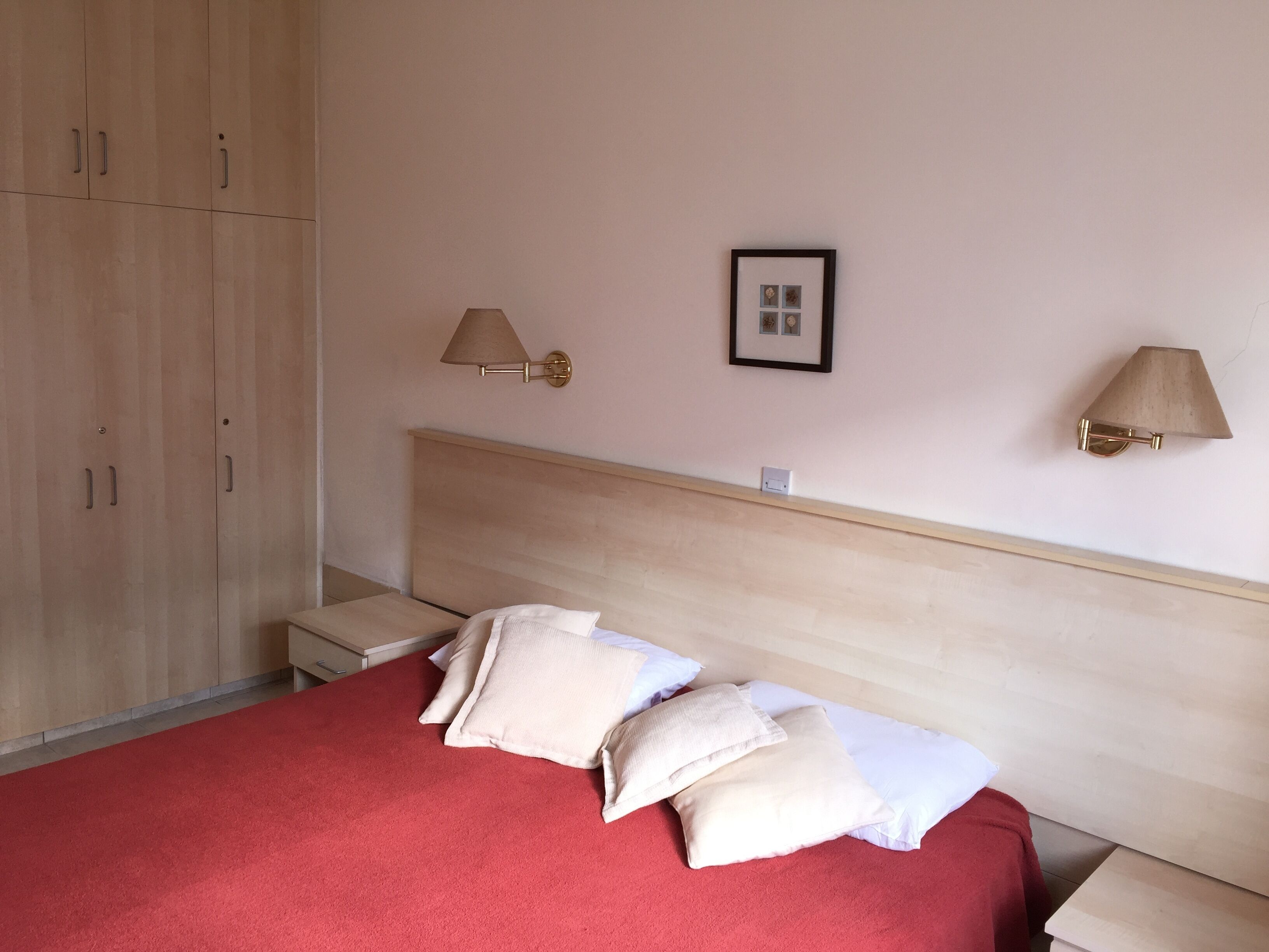 A bedroom with a bed, two bedside tables, a wardrobe, and two wall-mounted lamps.