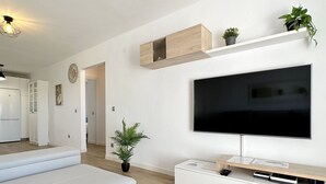 Ein modernes Wohnzimmer mit Flachbildfernseher, weißen Sofas, einem Holztisch und einem Topf mit Pflanze.