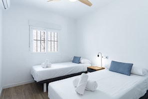 Ein Hotelzimmer mit zwei Einzelbetten, einem Nachttisch mit Lampe, einem Fenster mit Gitterstäben und einem Deckenventilator.
