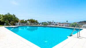 Una piscina rectangular con un borde de baldosas blancas, rodeada por una valla blanca, y un cielo azul despejado arriba.