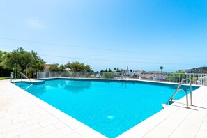 A rectangular swimming pool with a white tiled deck, surrounded by a white fence, and a clear blue sky above.