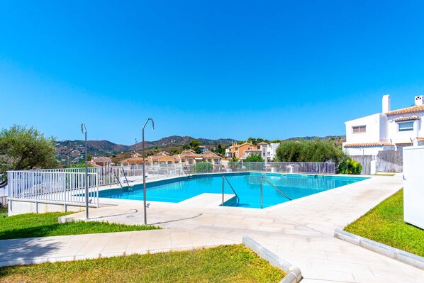A swimming pool with a white fence, surrounded by a paved area and greenery.