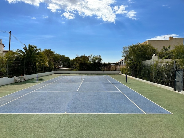 Ein Tennisplatz im Freien mit Netz, umgeben von Grünflächen und Gebäuden.