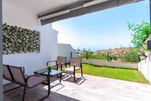 A balcony with a table and chairs, a view of a cityscape, and a white wall with a climbing plant.