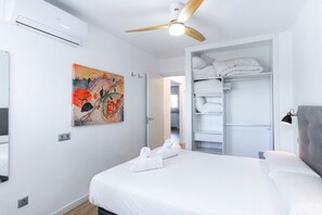 A hotel room with a bed, a ceiling fan, a painting, a wardrobe, and a bathroom visible through an open door.