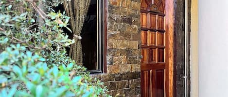 Edificio de piedra con puerta y ventana de madera, rodeado de vegetación.