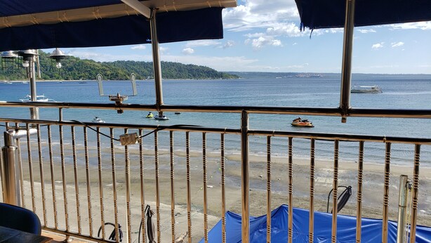 A balcony with a view of the sea, a sandy beach, and a distant green hill.