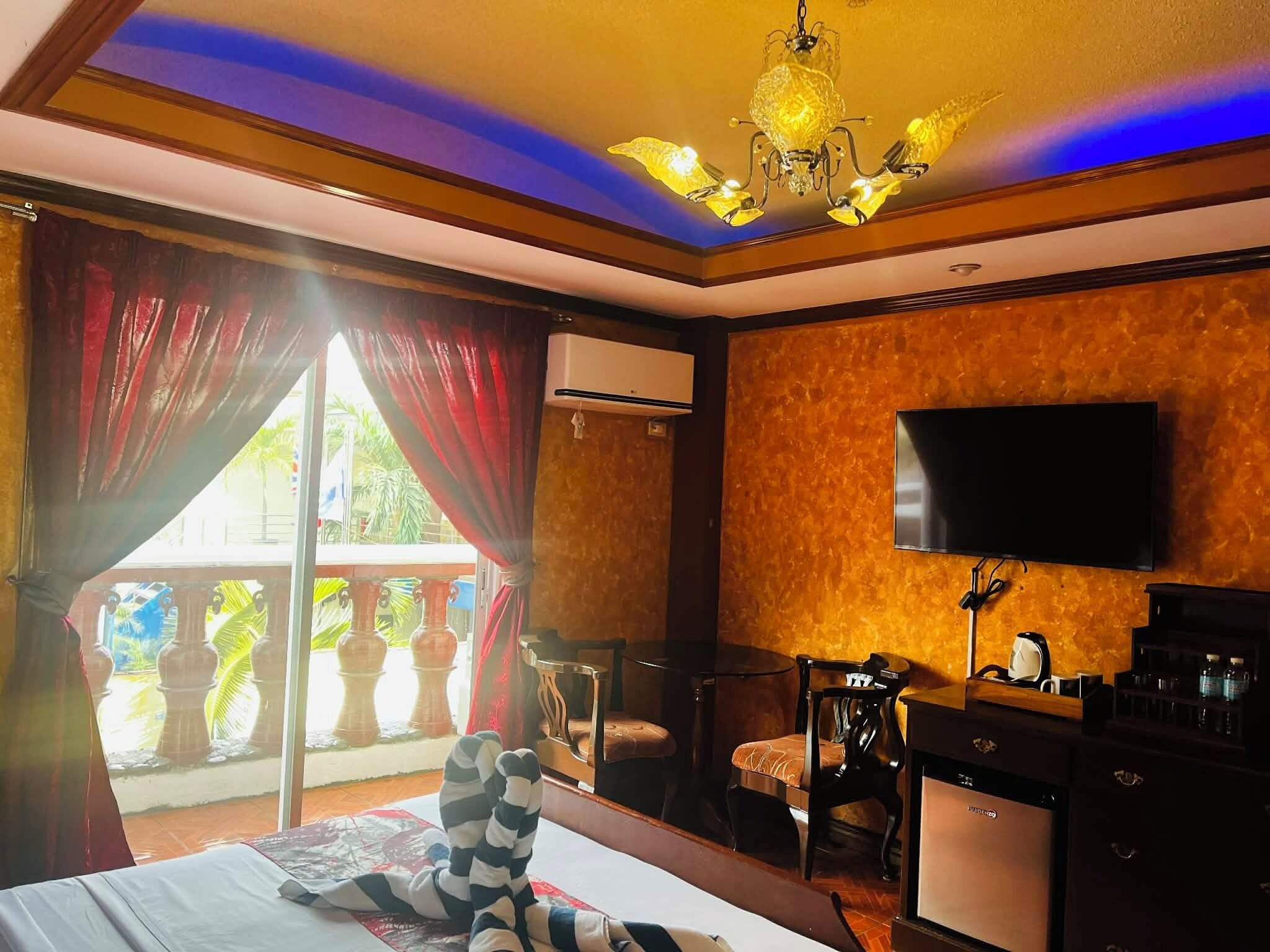 A hotel room with a bed, a desk, a chair, a television, and a balcony with curtains.