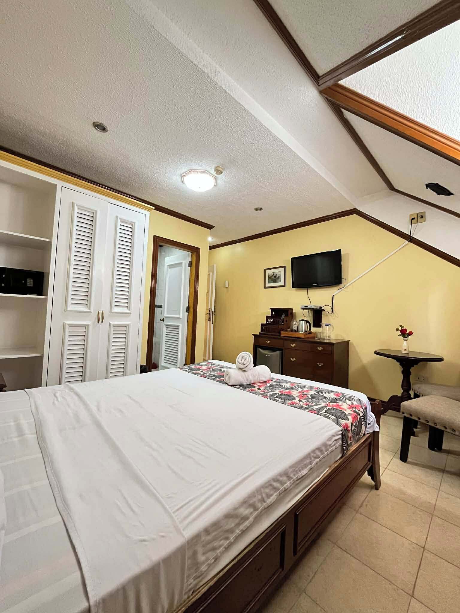 Un dormitorio con cama, armario, escritorio, silla y televisor en la pared.