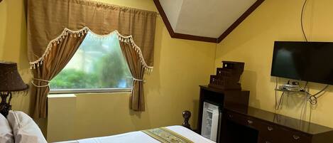 A hotel room with a bed, a television, a desk, and a window with curtains.