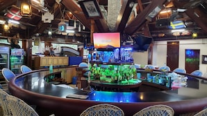 A bar area with a curved counter, wicker chairs, and a television screen displaying 'COLOR, COLD HEART'.