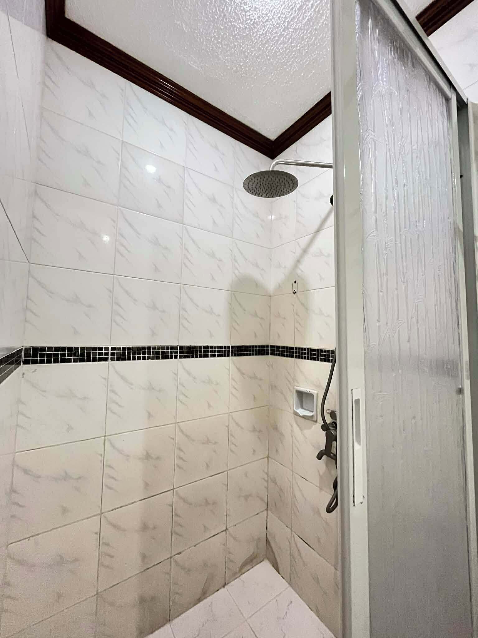 A shower with white marble tiles, a black tile border, and a showerhead.
