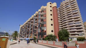 Un hotel de varios pisos con balcones, un patio central y un cielo azul despejado.