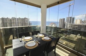 A dining table set with plates, glasses, and cutlery on a balcony with a view of the sea and buildings. - A21 LARIMAR 14ºB (Calpe)
