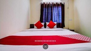 Habitación de hotel con cama, cortinas y una colcha roja y blanca.
