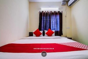 Habitación de hotel con cama, cortinas y una colcha roja y blanca.