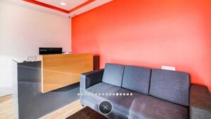 Una zona de recepción con un escritorio de madera, un sofá gris y una pared de acento roja.