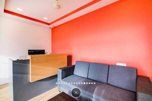 A reception area with a wooden desk, a grey sofa, and a red accent wall.