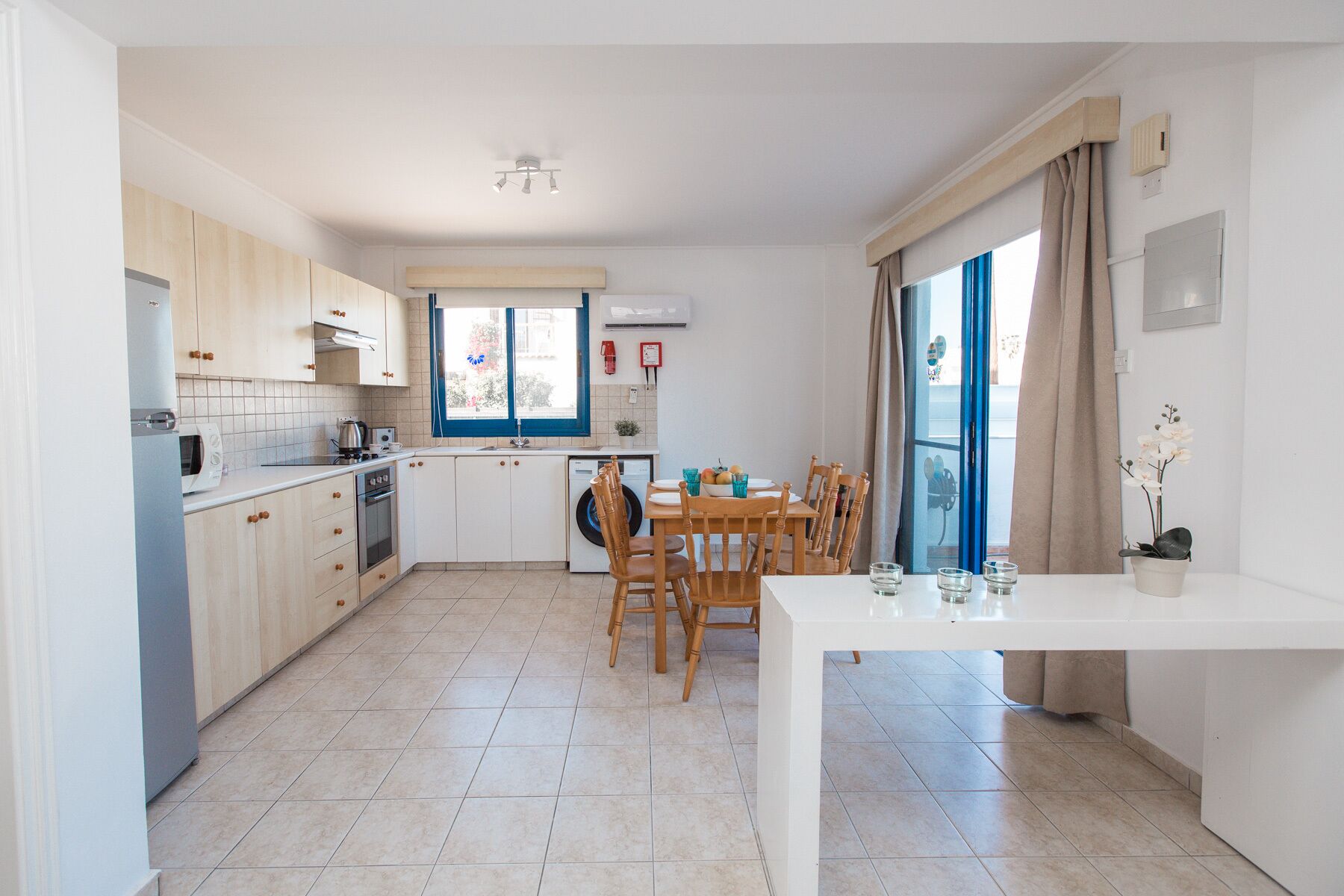 A modern kitchen with a dining area, featuring a large window, a built-in oven, and a dining table with chairs.