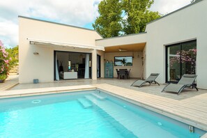 A modern outdoor pool area with a covered patio, lounge chairs, and a dining area.