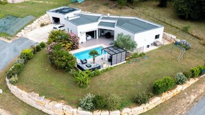 Une maison moderne à deux étages, dotée d’une piscine, d’un patio et d’un mur de soutènement en pierre.