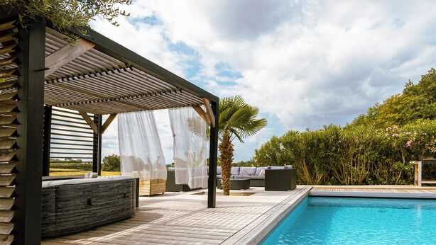Une terrasse en bois avec une piscine, un espace salon extérieur et un coin abrité agrémenté de rideaux légers.