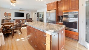 A modern kitchen with wooden cabinets, stainless steel appliances, and a granite countertop. - Of Wine & Gods - Hot Tub, BBQ and Fire Pit (Joshua Tree)