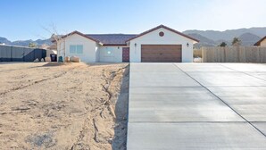 A residential house with a garage, a driveway, and a fenced yard. - Of Wine & Gods - Hot Tub, BBQ and Fire Pit (Joshua Tree)