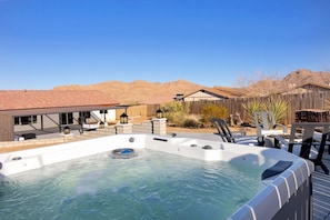 A hot tub with a wooden deck, surrounded by outdoor furniture and a wooden fence. - Of Wine & Gods - Hot Tub, BBQ and Fire Pit (Joshua Tree)