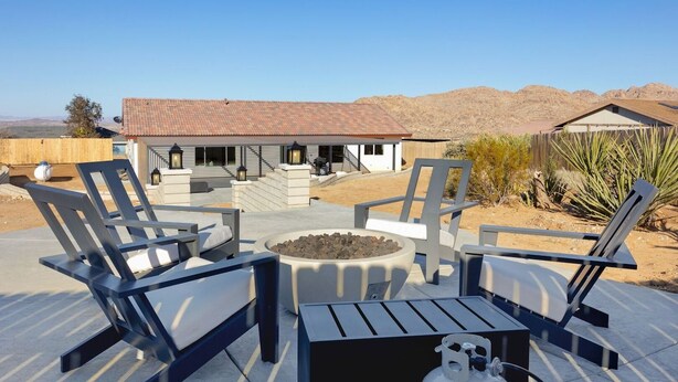 An outdoor patio with lounge chairs and a fire pit, a house with a tiled roof, and a desert landscape in the background.