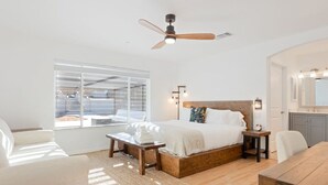A bedroom with a bed, bedside tables, a ceiling fan, a window, and a view of the outside.