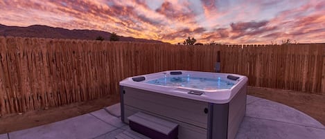 A hot tub in a backyard with a wooden fence and a sunset in the background.