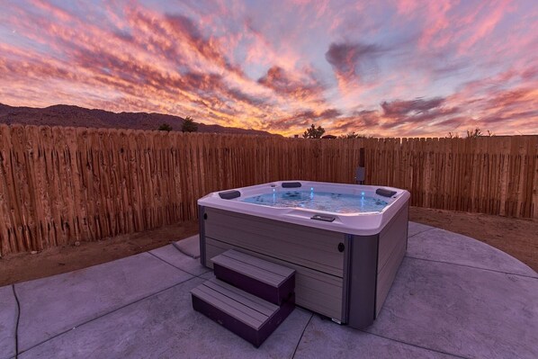 Un jacuzzi en un patio trasero con cerca de madera y un atardecer de fondo.