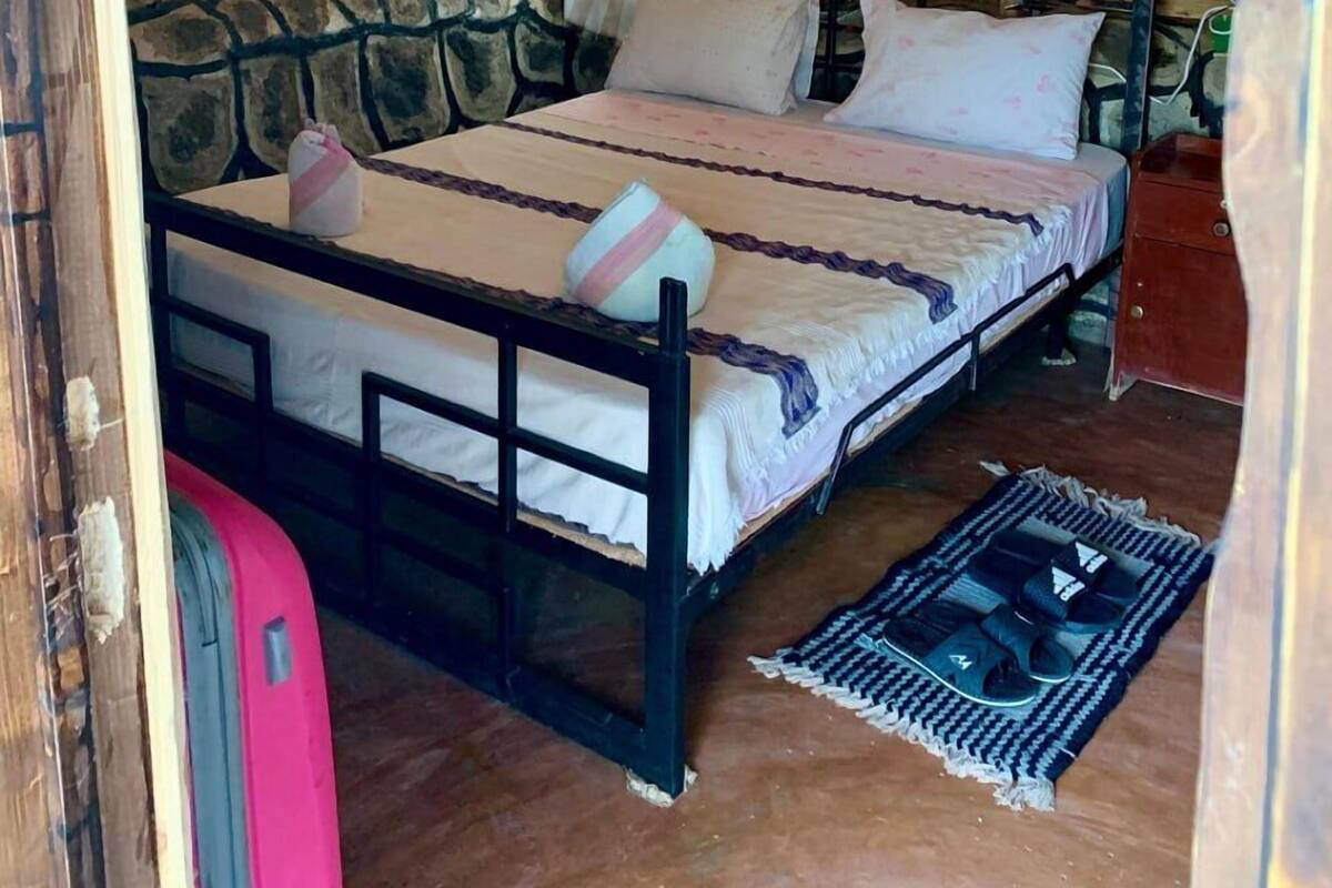 A rustic wooden room with a bed, a hanging mosquito net, and a suitcase.