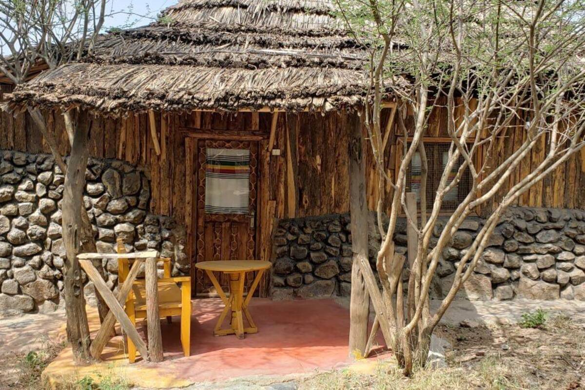 A rustic hut with a thatched roof, stone walls, and a wooden table and bench outside.