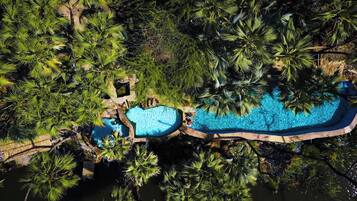 An aerial view of a resort with two swimming pools surrounded by dense tropical vegetation.
