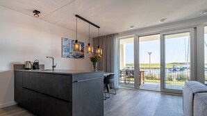Una cocina moderna con una isla central, iluminación colgante y vistas al exterior a través de amplios ventanales correderas.