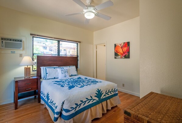 Un dormitorio con cama, mesita de noche, lámpara, ventilador de techo, ventana con persianas y aire acondicionado de pared, además de un cuadro.