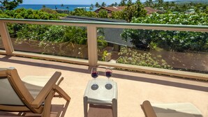Ein Balkon mit zwei Stühlen und einem kleinen Tisch, mit Blick auf einen üppigen Garten und die Küste.