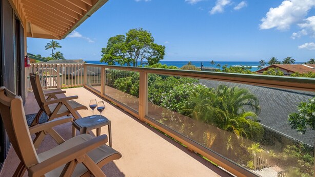 Ein Balkon mit Holzkufen und einem Tisch, mit Blick auf die Küste, Palmen und das Meer.