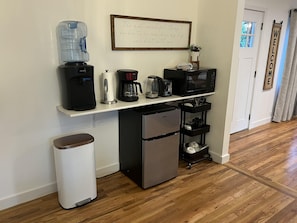 En kompakt tekøkken med vanddispenser, kaffemaskine, mikrobølgeovn og minikøleskab.