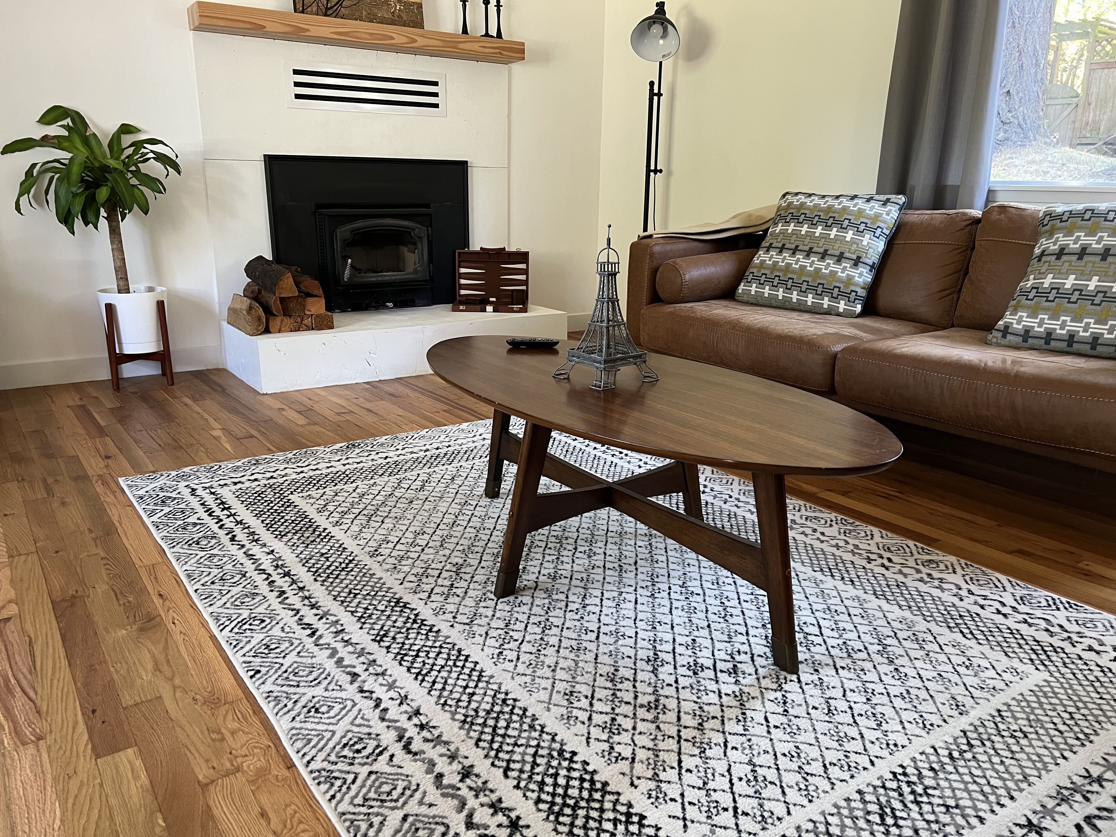 A living room with a fireplace, a brown leather sofa, patterned rugs, and a wooden coffee table.