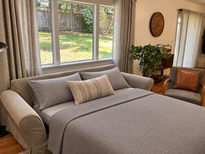 Une chambre avec un grand lit, une fenêtre, une horloge et une plante.