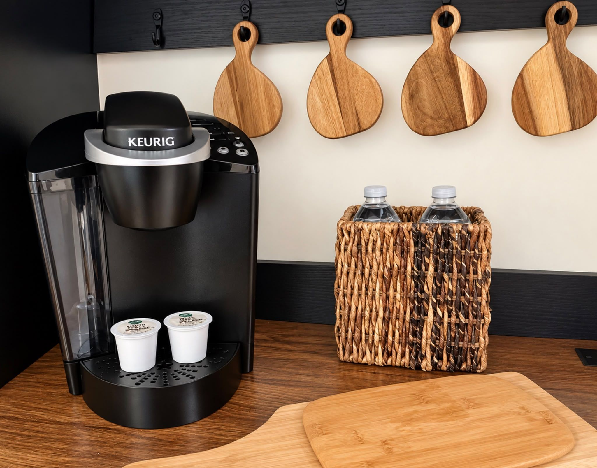 A modern kitchen with a Keurig coffee maker, two cups, and a woven basket with water bottles.