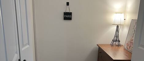 Una habitación con piso de madera, un escritorio con cajones, una lámpara y un cartel con la palabra 'PARIS' en la pared.