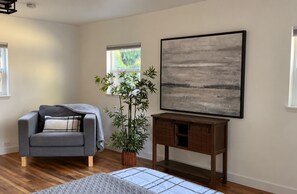 Een kamer met een grijze bank, een potplant, een houten bijzettafeltje en een groot abstract schilderij aan de muur.
