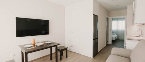 Una sala moderna con un televisor de pantalla plana, una mesa de comedor, un sofá y una zona de cocina con refrigerador.