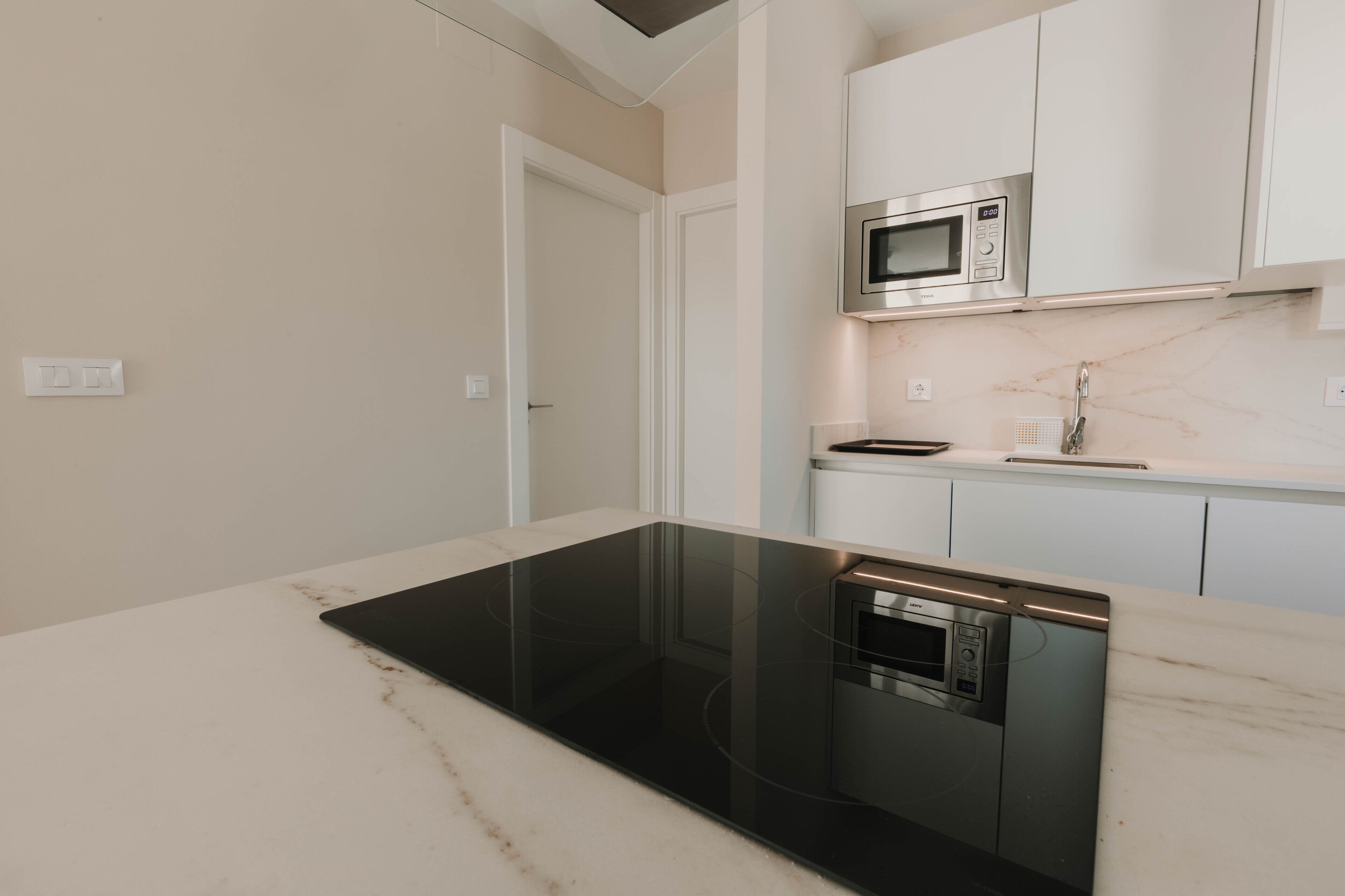 A modern kitchen with a black induction cooktop, a built-in oven, and a microwave.